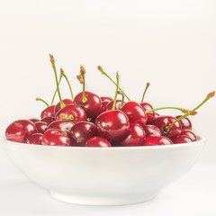 Ripe cherry lies in a white bowl on a white background