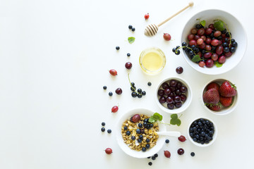 Bowl of homemade granola with strawberry, blueberry, cherry, gooseberry, black currant and honey on white wooden background. Top view. Flat lay. Copy space