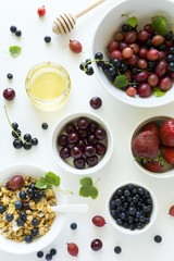 Bowl of homemade granola with strawberry, blueberry, cherry, gooseberry, black currant and honey on white wooden background. Top view. Flat lay. Copy space