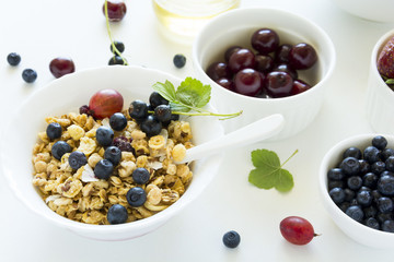 Bowl of homemade granola with strawberry, blueberry, cherry, gooseberry, black currant and honey on white wooden background. Top view. Flat lay. Copy space