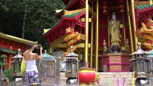 A woman is photographing a statue of a deity in a Buddhist temple
