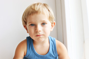 Close up portrait of cute blond blue eyed three year old boy wearing tank top, looking sad. Unhappy...