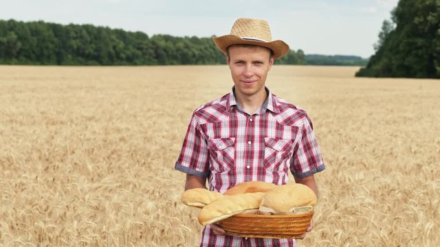 Happy farmer hold a basket with bakery products standing in the middle of a ripe wheat field. Front view. Slow motion
