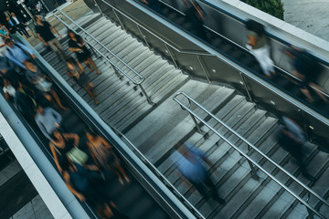 People on stairs and moving escalator at the interchange station near business and commercial center in Paris. Urban scene, city life, public transport hub and traffic concept. Blurred background
