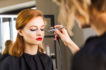 Visagiste making the girl professional makeup using an airbrush.