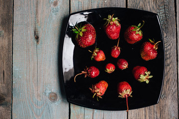 top view Red ripe strawberries on a black plate on a wooden table top view