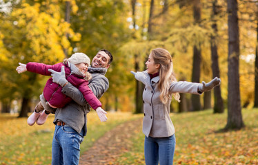 Naklejka na ściany i meble family, season and people concept - happy mother, father and little daughter playing at autumn park