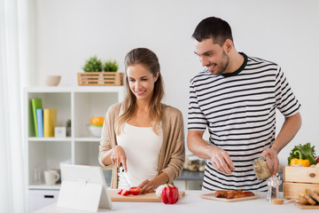 people and healthy eating concept - happy couple with tablet pc computer cooking food at home kitchen
