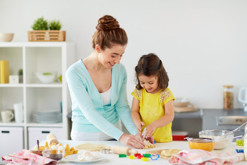 Fototapeta premium family, cooking and people concept - happy mother and little daughter with molds making cookies from dough at home kitchen