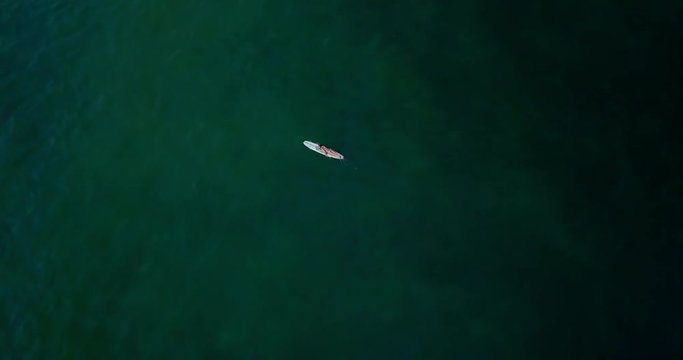 Beautiful surfer lady in sexy bikini with surfing longboard. Girl sit on her long board in ocean and wait her wave. Modern lifestyle. People water sport camp. Extreme vacation. Aerial drone footage.