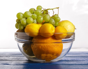 Fruit in a glass container on a green wooden table on a white background.
