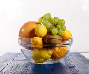 Fruit in a glass container on a green wooden table on a white background.