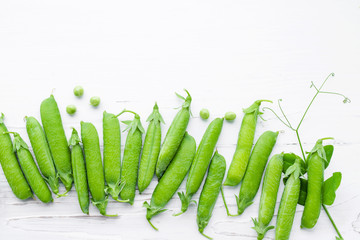 Pods of green peas on a white wooden surface close up, top view, copy space