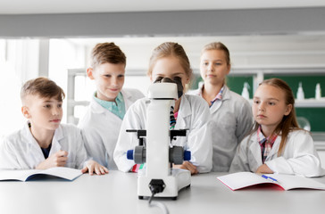 Fototapeta premium education, science and children concept - kids or students with microscope studying biology at school laboratory