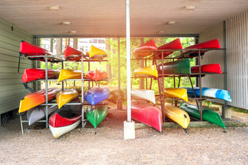 Collection of vibrant colorful plastic recreational canoe and kayaks stored storage rack, front view