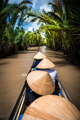 Rowing on a traditional boat with traditional hats on in a canal on Mekong Delta in Vietnam. - obrazy, fototapety, plakaty