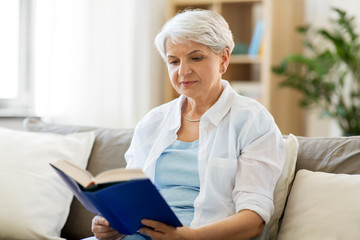 age, leisure and people concept - senior woman reading book at home