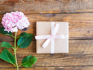 Geschenkspaket mit rosa Schleife und einer Blume auf einem Holztisch