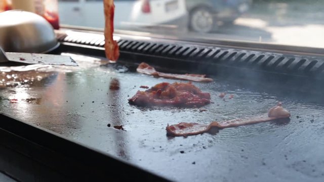 A Cook Puts The Bacon On The Grill For A Burger