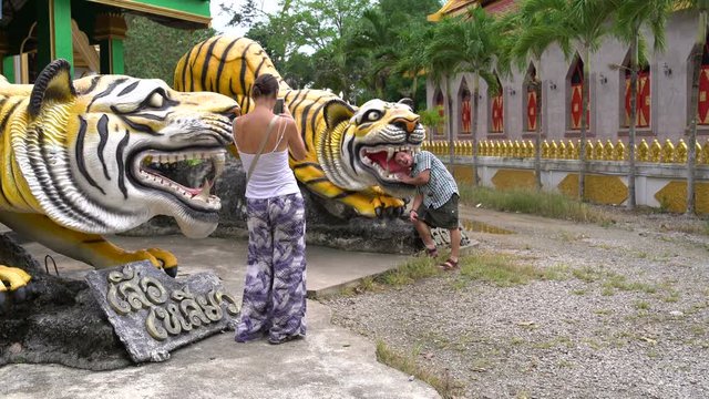 A woman is taking pictures of a man with a tiger statue.