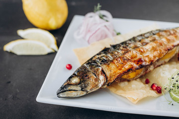 Fried fish in white plate with herbs and lemon, closeup.