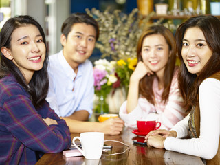happy young asian adults looking at camera smiling in coffee shop