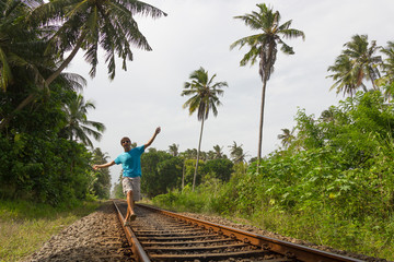 Young man walking on railroad track while listening to music with headphones on his smartphone in...