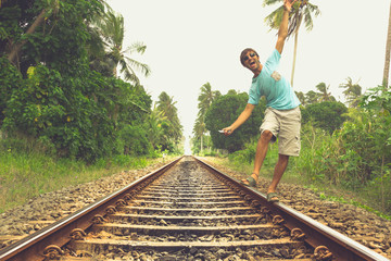 Young man walking on railroad track while listening to music with headphones on his smartphone in...