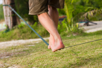 Close up on legs of man in shorts keeping balance while walking on slackline at the beach in the island of Koh Phangan, Thailand. Walk the line, equilibrium concepts