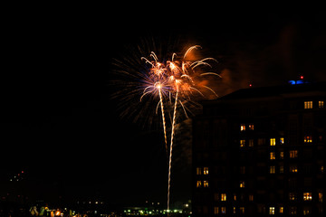 A Fourth of July fireworks display explodes over the waterfront in the city center of Norfolk Virginia, in the context of buildings, apartments, and dwellings
