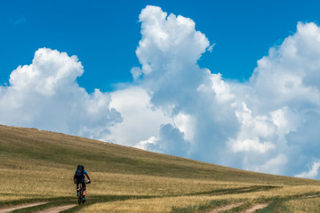 Cyclists riding along the steppe road with clouds