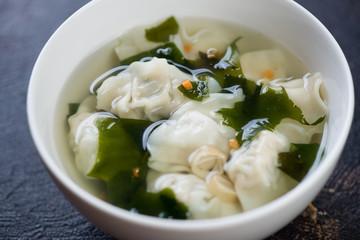 White bowl of chinese soup with wonton dumplings, close-up, horizontal shot