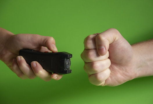 Electroshocker in the hand of a woman and the fist of the intruder on a green background, Methods of self defense, danger