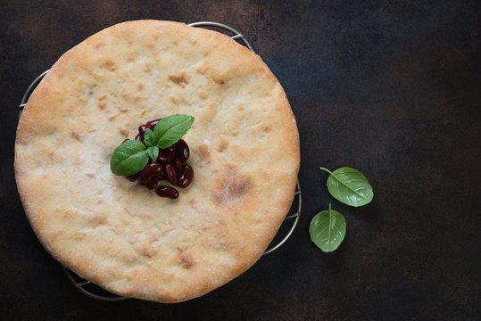 Georgian traditional flatbread lobiani stuffed with red beans, flatlay over dark brown metal surface with space