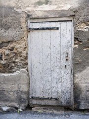 very old white painted peeling grungy door in ancient wall of medieval house in village of french provence