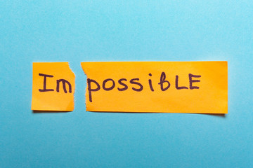 The word impossible is written on yellow paper and torn on a blue background