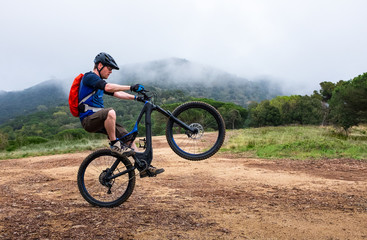 Obraz premium Young man doing a wheelie on a black and blue electric mountain bike