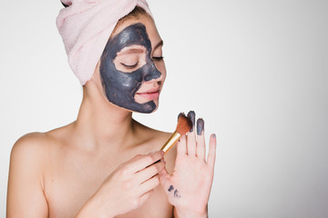 charming young girl with a towel on her head applies a useful clay mask to half the face with a...