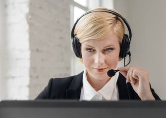 Concentrated call center operator, blonde woman dressed in black jacket and white shirt working on...