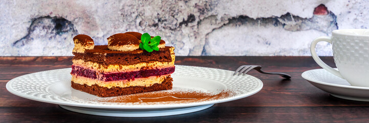 Panoramic view on tiramisu on a white plate with cocoa and fresh mint, a fork and a cup of coffee