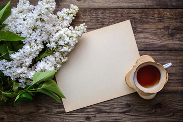 White Terry Persian lilac, a cup of tea and a sheet of paper on a wooden background