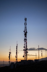 communication tower. cell, radio and television antennas on top of a mountain and below a lit coastal village