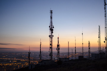 communication tower. cell, radio and television antennas on top of a mountain and below a lit coastal village - obrazy, fototapety, plakaty