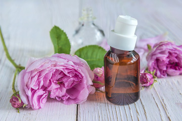 Pink rose flowers and dark vial with essential oil on the white paint wooden background