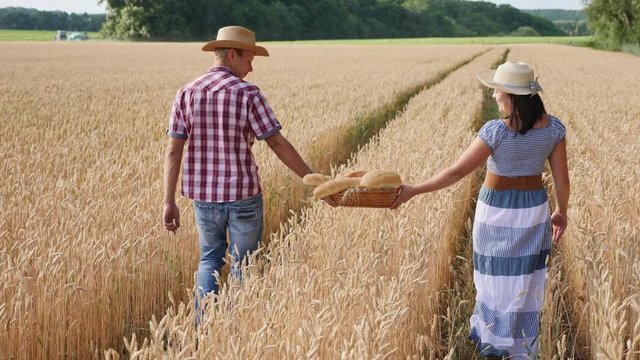 Man and woman farmers carry in the basket bread, bakery products walking along the ripe wheat field. Slow motion steadicam shot