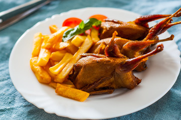 Roasted quails and potatoes served in a white plate on table