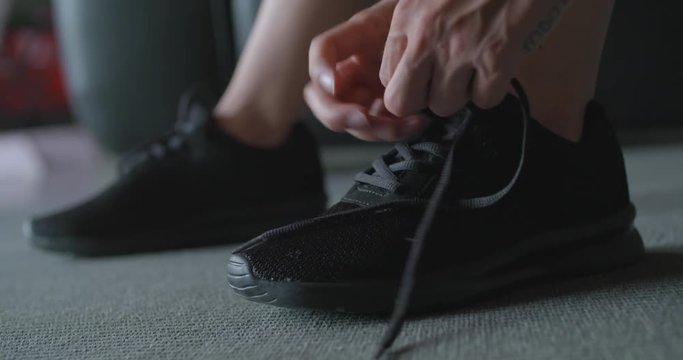 tattooed woman tying her shoes before fitness sport workout at home. Legs and shoes detail. .Living room domestic training. 4k slow motion video