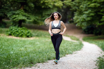 Girl runs to the park. A young woman runs along a path in the green of the natural park. Daylight, summer, among the trees of a public garden.