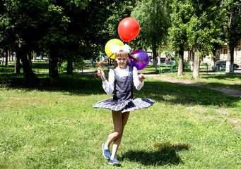 A teenage girl, whirls and dances in a green glade, holds a multicolored hands, air balloons