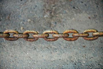 Old oxidized rusty chain hanging over asphalt close up with copy space. Conceptual background with thick links of strong chain. Artwork.